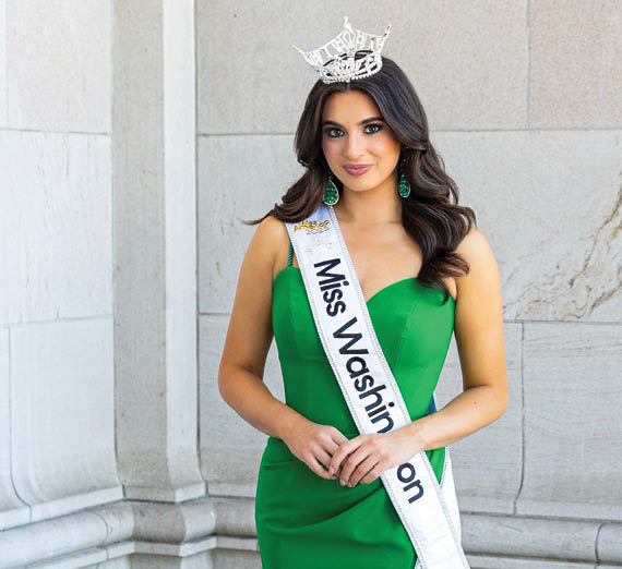 A man with a beard and tattooed arms stands with his arms crossed